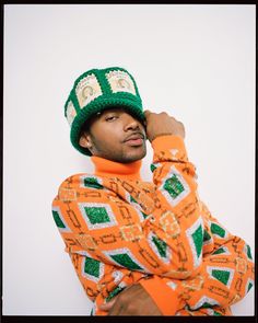 a man in an orange shirt and green hat is posing for the camera with his hands on his head