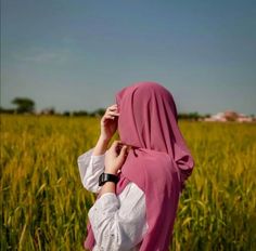 a woman in a pink hijab is standing in a field with tall grass