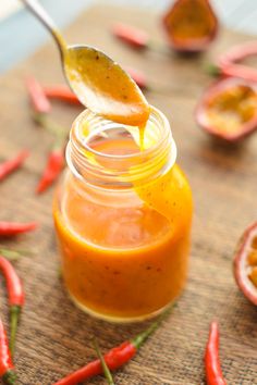 a spoon full of sauce sitting on top of a wooden cutting board next to peppers