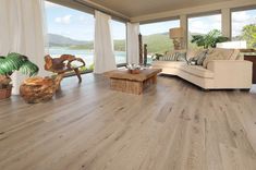 a living room with wood flooring and large windows looking out onto the water in the distance