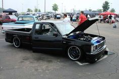 a truck with its hood open parked in a parking lot next to other cars and people