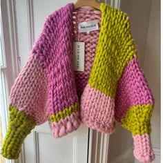 a pink, yellow and green sweater hanging on a door