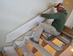 a man sitting on top of a wooden step next to a white stair case in a house