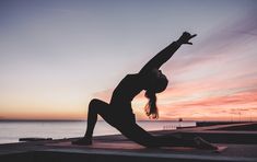 a woman doing yoga in front of the ocean at sunset with her arms stretched out