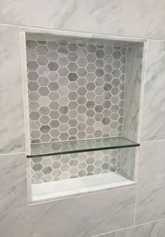 a glass shelf in the corner of a tiled shower wall with hexagonal tiles