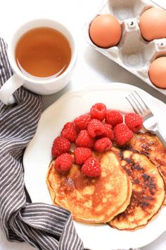 pancakes with raspberries and syrup on a plate next to an egg carton