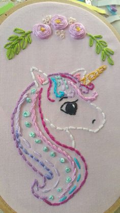 a close up of a embroidery on a piece of cloth with a unicorn face and flowers