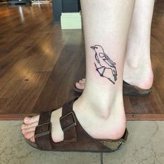 a small bird tattoo on the foot of a woman's right foot, which is sitting on top of a wooden floor