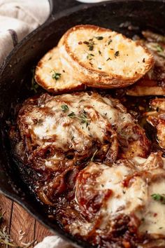 an iron skillet filled with meat covered in gravy and garlic bread slices