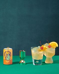 two cocktails and an orange juice can on a green table with a blue background