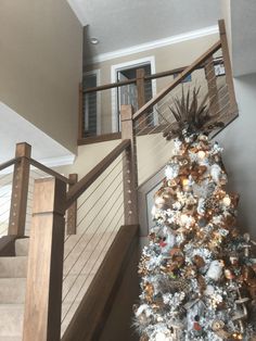 a christmas tree with lights and ornaments on it in the middle of a room next to stairs