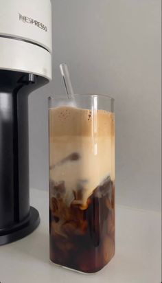 an iced drink in a glass next to a coffee maker