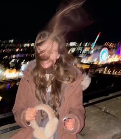 a girl is spinning her hair in front of the city at night with lights behind her