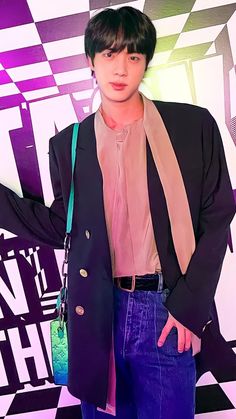 a young man wearing purple pants and a black blazer is standing in front of a colorful background