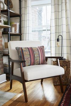 a chair with a pillow on it sitting in front of a window next to a book shelf