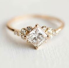 a gold ring with a princess cut diamond surrounded by small white diamonds on the side