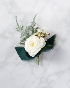 a boutonniere with white flowers and greenery on a marble surface, top view