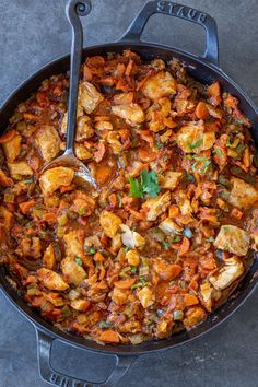 a pan filled with chicken and carrots on top of a table next to a spoon