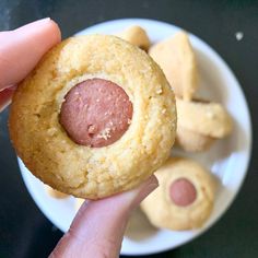 a person holding up a cookie with a sausage in it's center and other food on the side