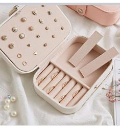 an open jewelry box on top of a white sheet with pearls and other accessories in it