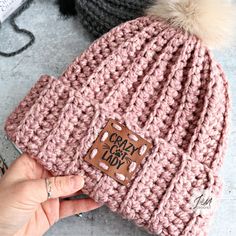 a hand is holding a pink knitted beanie with a brown patch on it