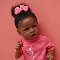 a baby doll with a pink shirt and bow on it's head standing against a pink wall