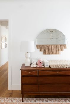 a dresser with a mirror, lamp and stuffed animals on it in a white room