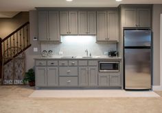 a kitchen with gray cabinets and stainless steel refrigerator freezer next to an open staircase