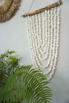 a white beaded necklace hanging on a wall next to a plant and straw hat