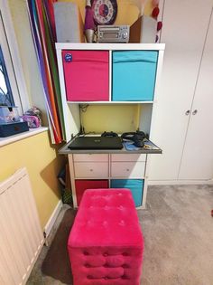 a pink ottoman sitting in front of a white book shelf filled with colorful bins