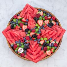 a bowl filled with watermelon, grapes and strawberries on top of a marble counter