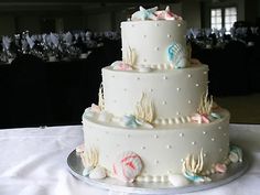 a three tiered wedding cake with seashells and starfish on the side