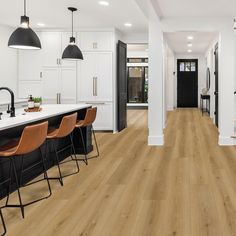 an open kitchen and dining room with white walls, wood flooring and black accents