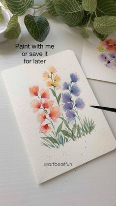 two cards with watercolor flowers on them next to some green leaves and a plant