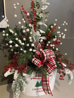 a christmas arrangement in a bucket with red berries and greenery on the top, sitting on a table