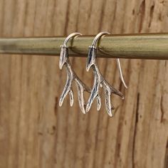 three small silver leaves hang from a wooden stick on a wood background, one is dangling from the end of a pair of earrings