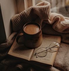 an open book with glasses on it next to a cup of coffee