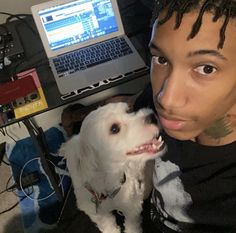 a young man with dreadlocks kissing his dog in front of a laptop computer