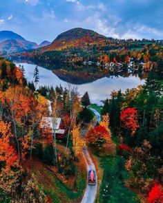 a car driving down a road next to a lake in the middle of trees with fall foliage