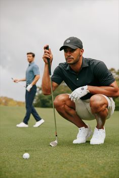 two men playing golf on a cloudy day, one holding a ball and the other squatting down