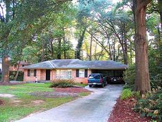 a car is parked in front of a house with trees around it and grass on the ground