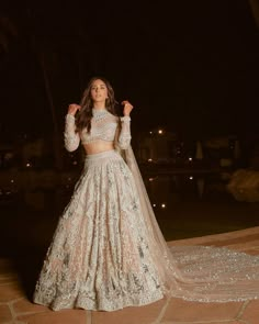 a woman in a white gown standing on a patio at night with her hands up