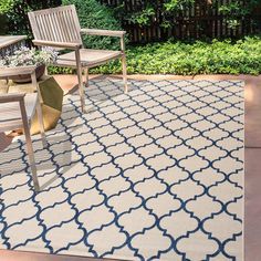 an outdoor area rug with chairs and plants in the background, on a patio surrounded by shrubbery