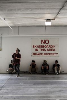 people sitting on the floor in a parking garage with a no skateboarding sign above them