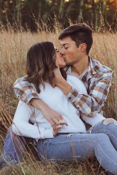 a man and woman sitting in tall grass kissing on the forehead while holding each other