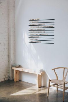 a wooden chair sitting in front of a white wall with writing on the wall behind it