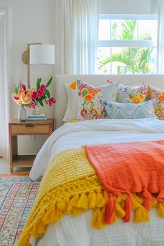 a white bed topped with lots of pillows next to a window