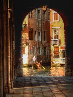 a person in a small boat on a canal under an arch with buildings and windows