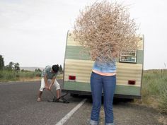 a woman standing in front of a trailer filled with dried plants next to another person