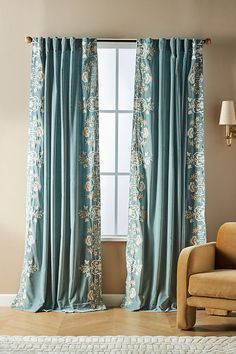 a living room with a chair and window covered in blue drapes next to a white rug